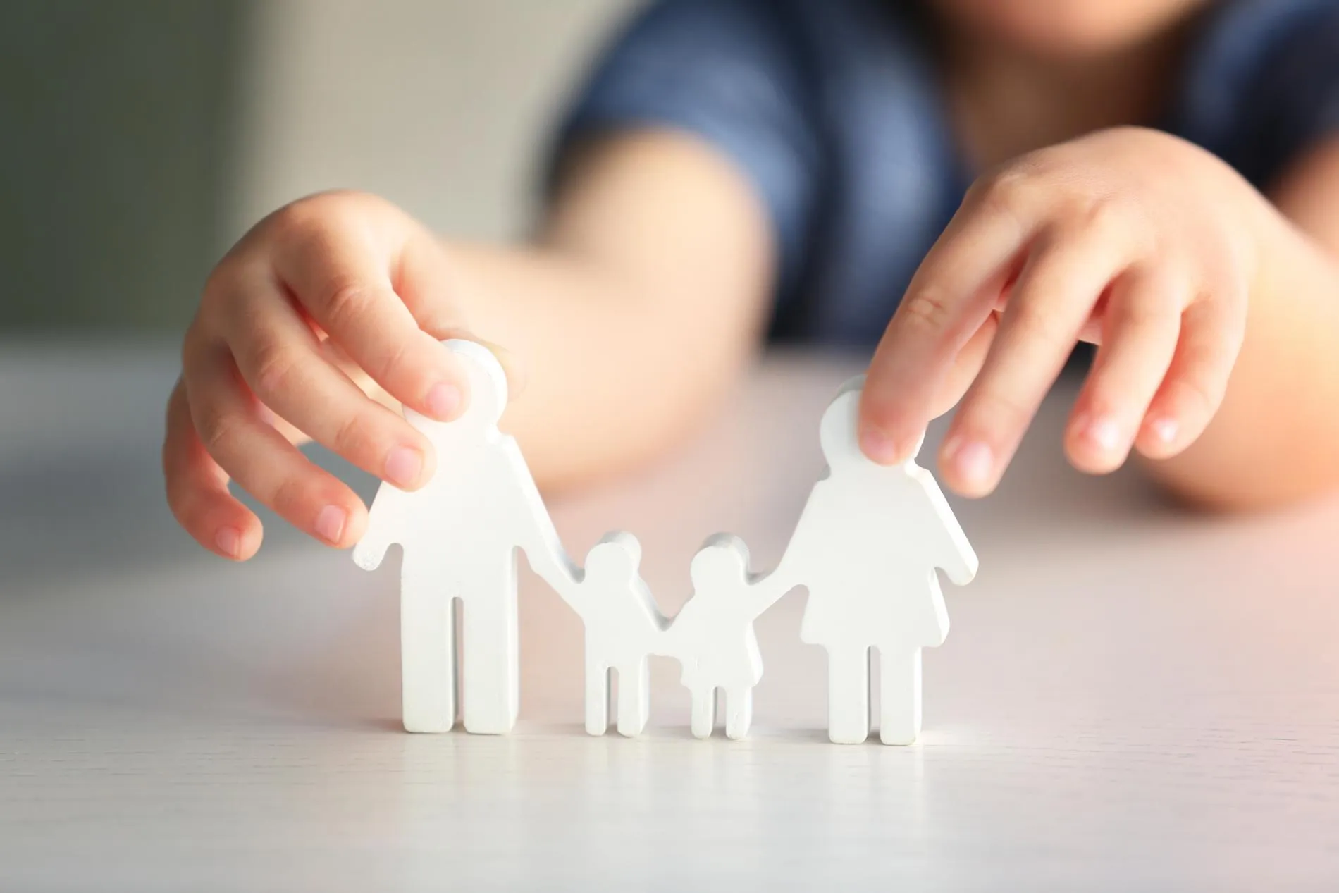 A child's hands interacting with a set of white, paper or plastic cutout figures representing a family