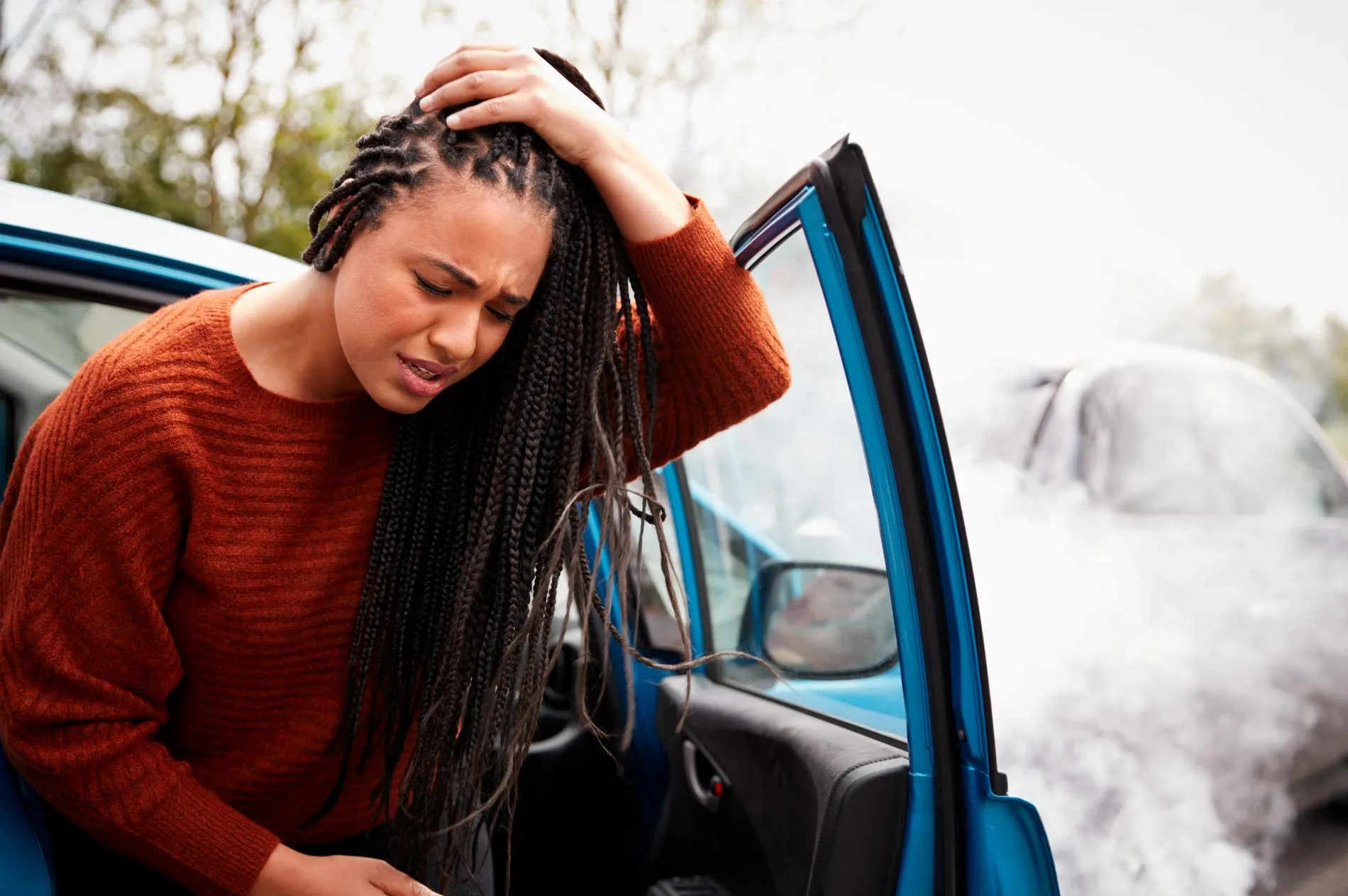 A woman stepping outside of a car holding her head in pain